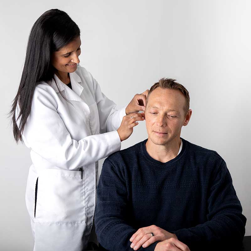 Audiologist  fitting a man with a hearing aid. 
